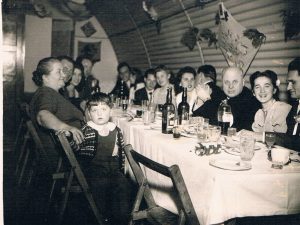 A photograph of an extended family seated around a large table in a Nissen hut celebrating a wedding reception